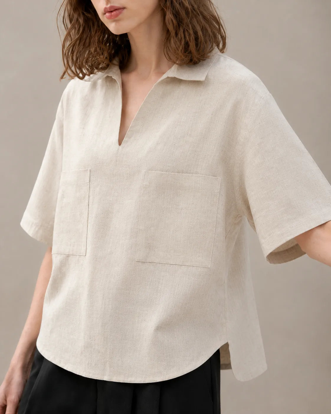 Close-up of the two patch pockets on an oversized linen beige V-neck shirt.