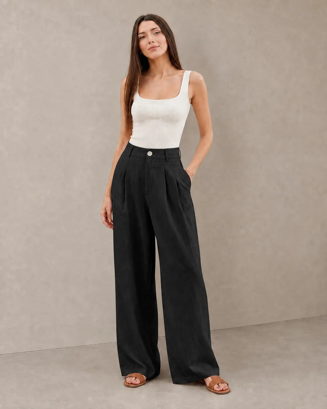 Model wearing black wide-leg summer trousers in a cotton-linen-polyester blend with a pleated high waist, styled with a ribbed white tank top, front view.
