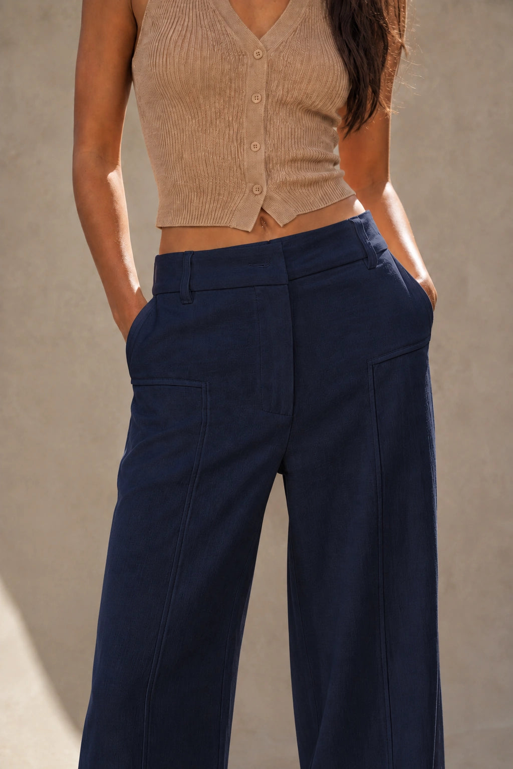 Close-up of the front waistband, belt loops and patch pockets on dark wide-leg linen-cotton trousers, styled with a cropped knit top.