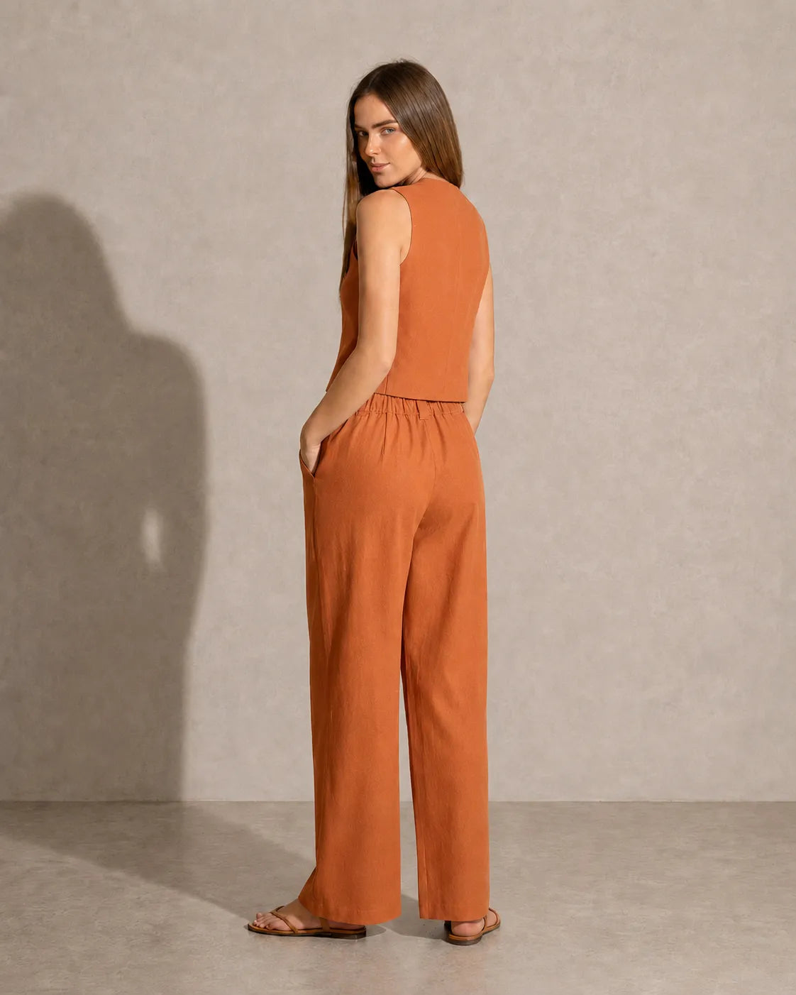 Achteraanzicht van een model in de oranje co-ord set, met zicht op de taillelband van de broek met lage taille.