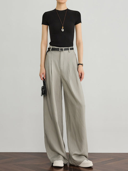 Model wearing light grey structured wide-leg tencel-linen trousers with a black t-shirt and a braided brown belt, a three-colour neutral combination, front view.