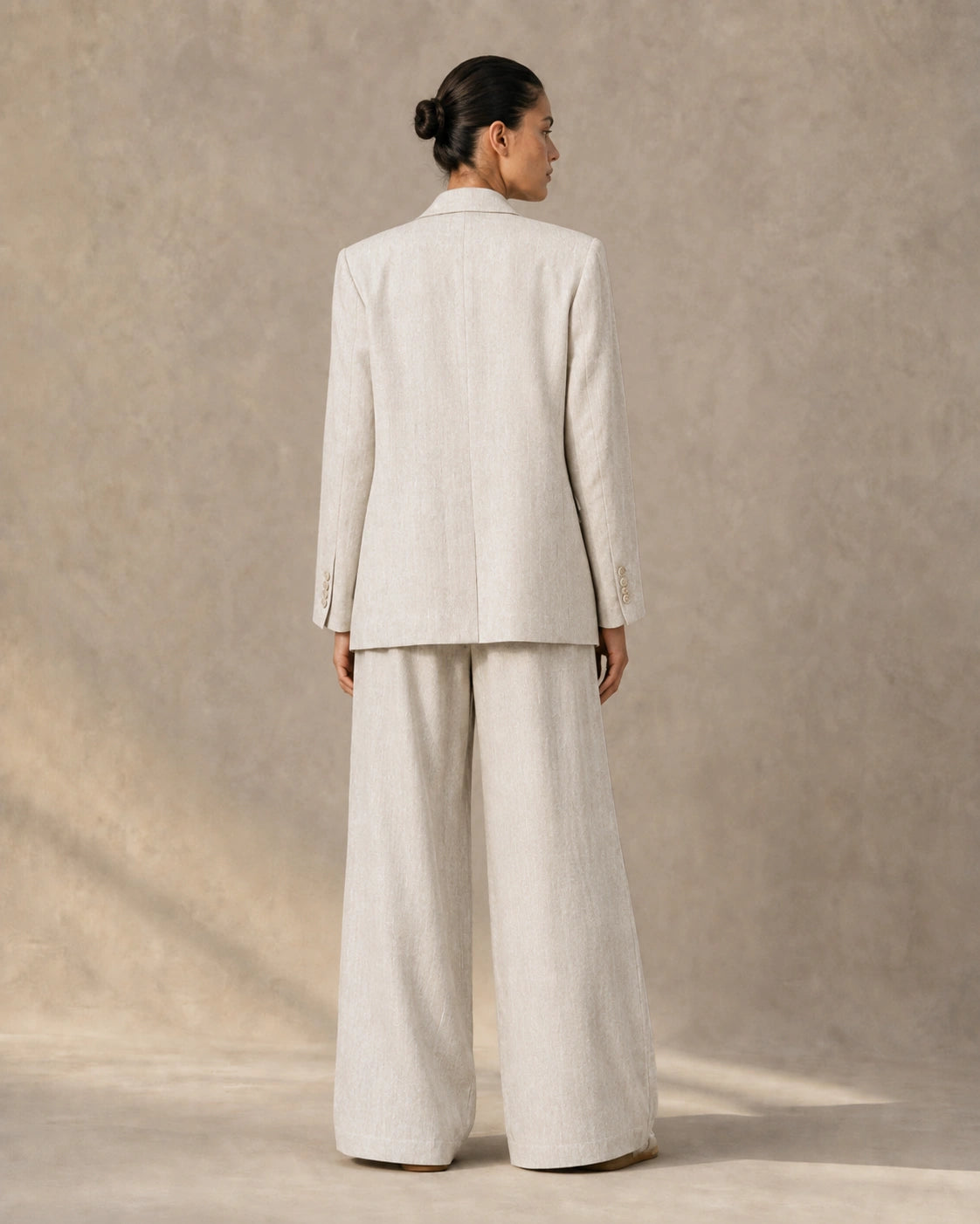 Back view of a model wearing the full apricot tencel-linen blazer and tailored trousers co-ord set.