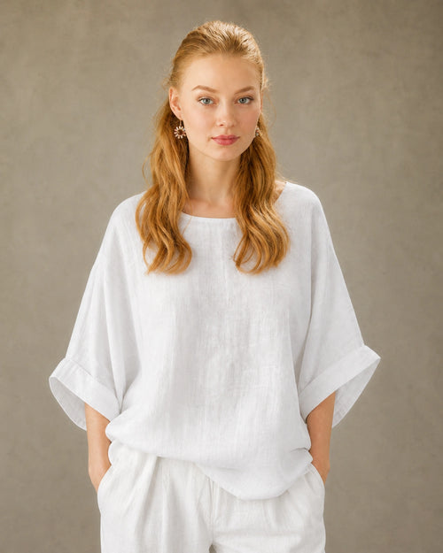 Vrouw draagt een wit bamboe-hennep blouse met ronde hals, valschouder en driekwart mouwen, vooraanzicht.