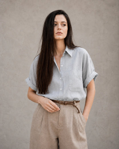 Vrouw draagt een lichtgrijs katoen-linnen blouse met polokraag en korte mouwen, vooraanzicht.