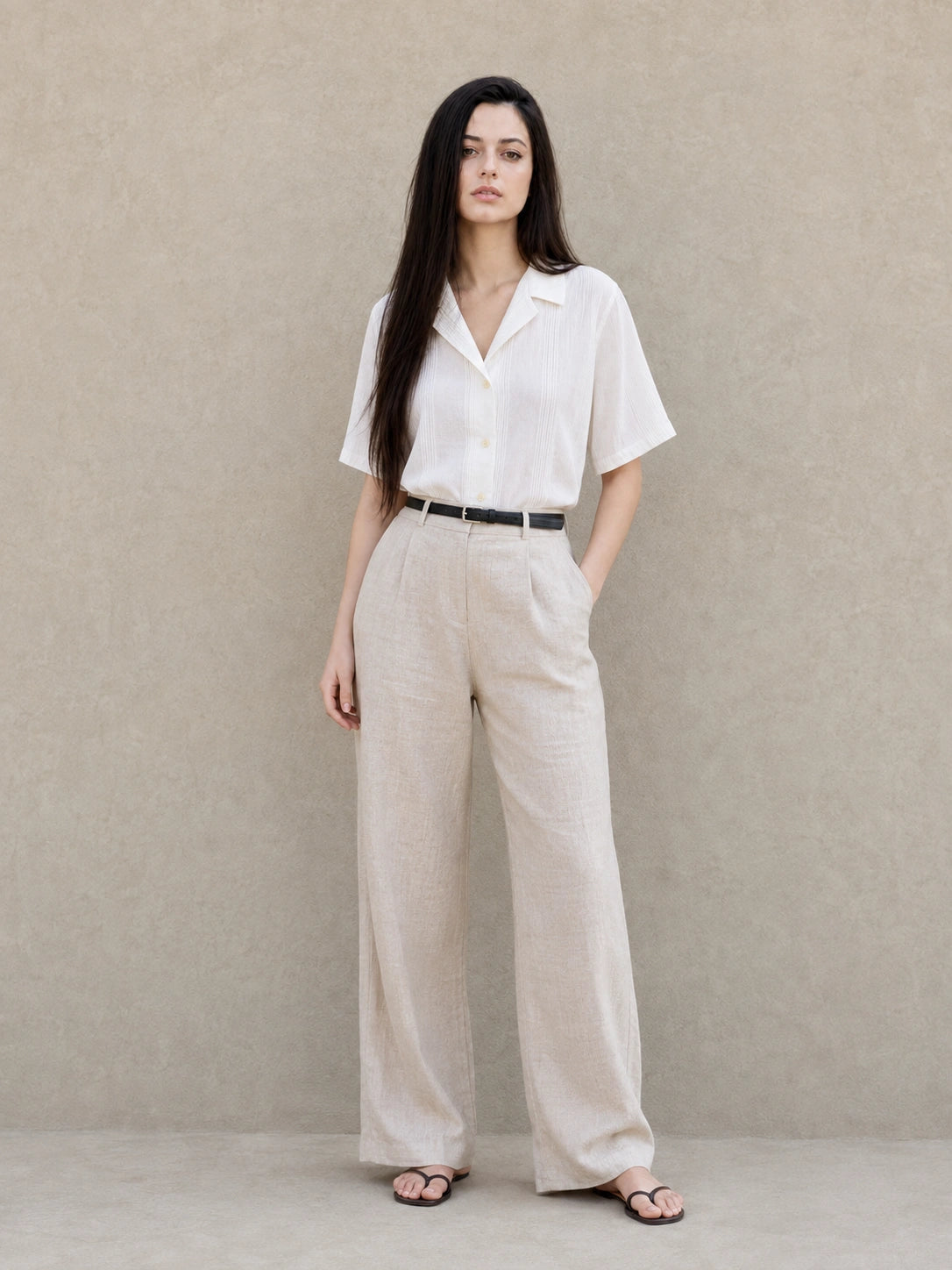 Volledige look van een vrouw in een witte blouse met Cubaanse kraag en korte mouwen, gecombineerd met een wijde beige broek.