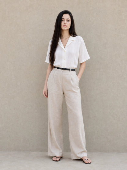 Volledige look van een vrouw in een witte blouse met Cubaanse kraag en korte mouwen, gecombineerd met een wijde beige broek.