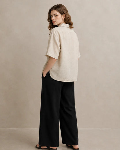 Three-quarter back view of a woman wearing an oversized linen beige V-neck shirt.