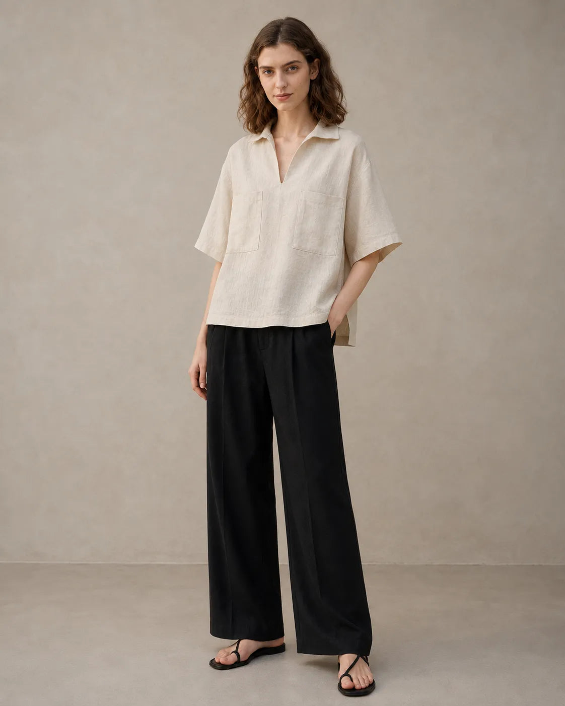 Full-length shot of a woman wearing an oversized linen beige V-neck shirt, styled with wide-leg black trousers.