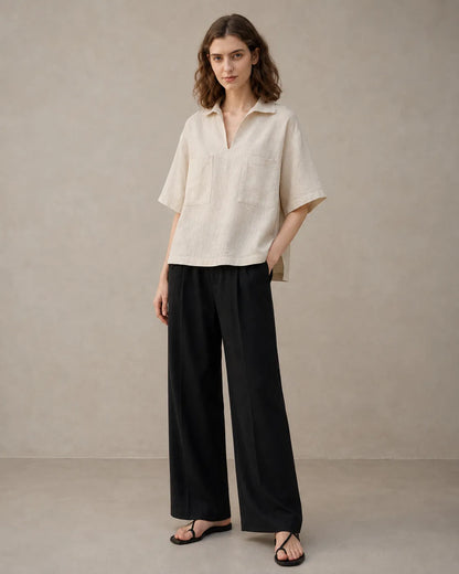Full-length shot of a woman wearing an oversized linen beige V-neck shirt, styled with wide-leg black trousers.