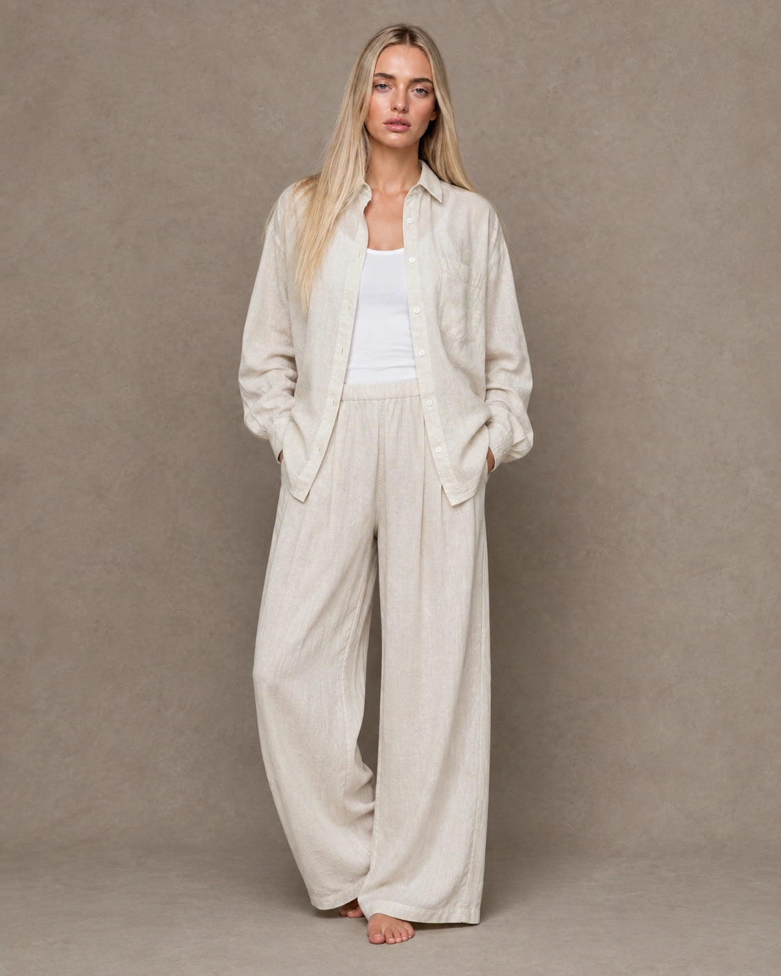 Full-length shot of a woman wearing a beige linen shirt open over trousers in a matching tone.
