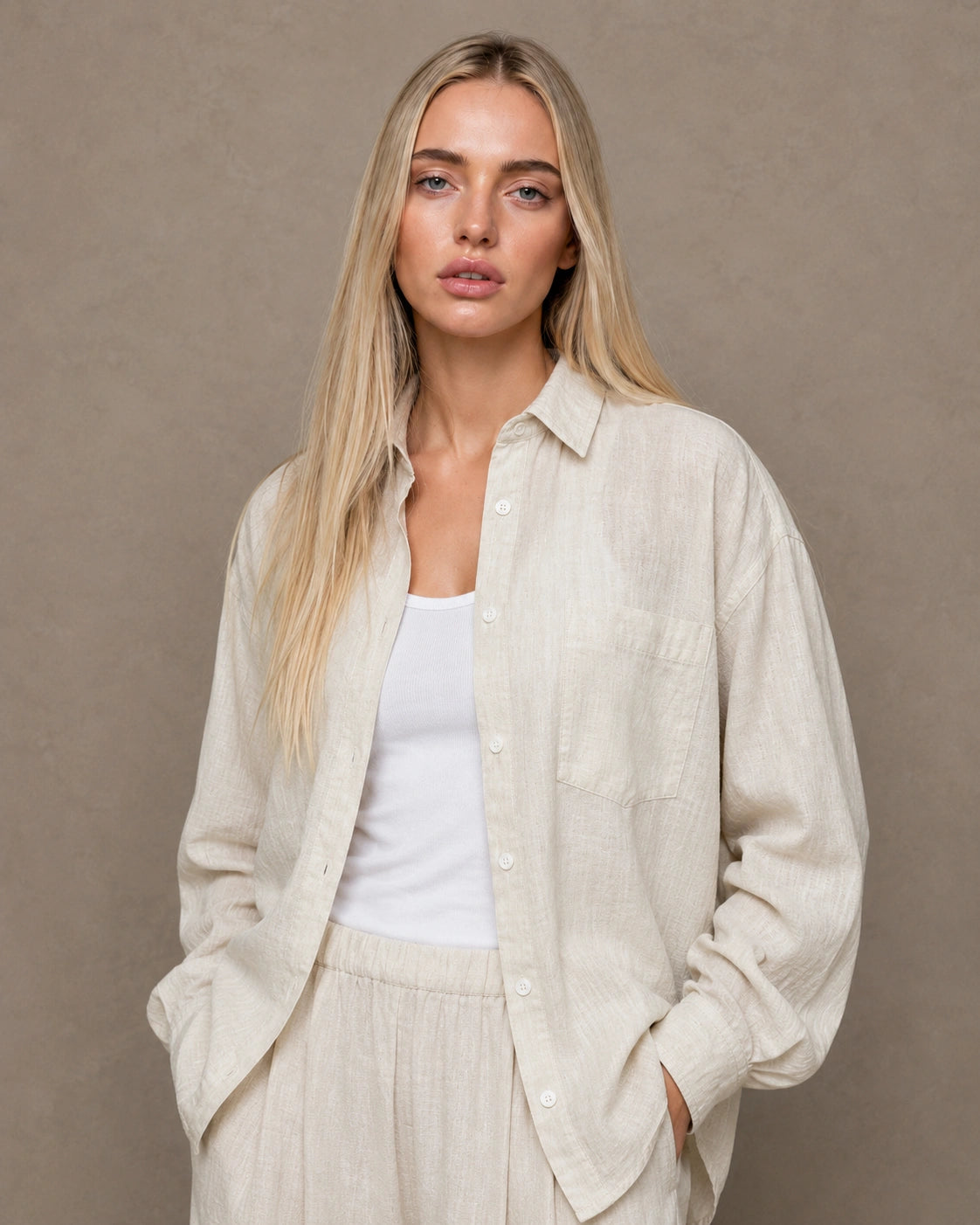 Woman wearing an open, cardigan-style beige linen shirt with a polo collar over a white camisole.