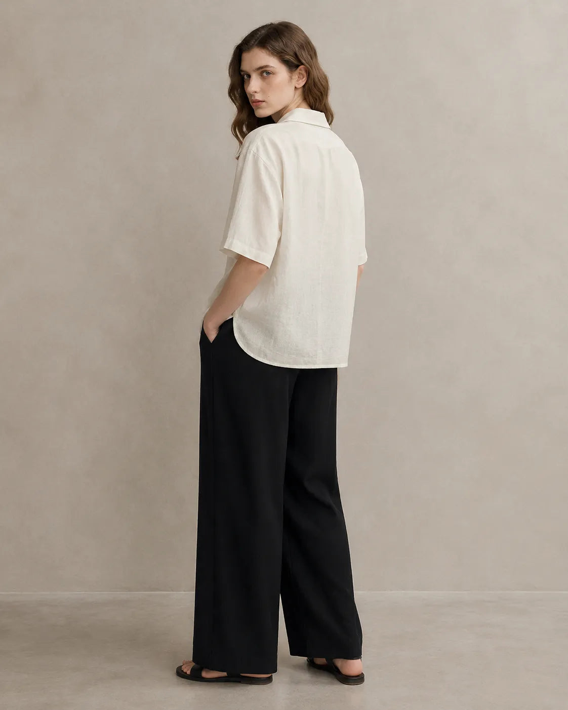 Three-quarter back view of a woman wearing an oversized off-white linen V-neck shirt.