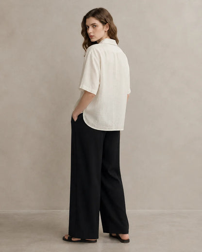 Three-quarter back view of a woman wearing an oversized off-white linen V-neck shirt.