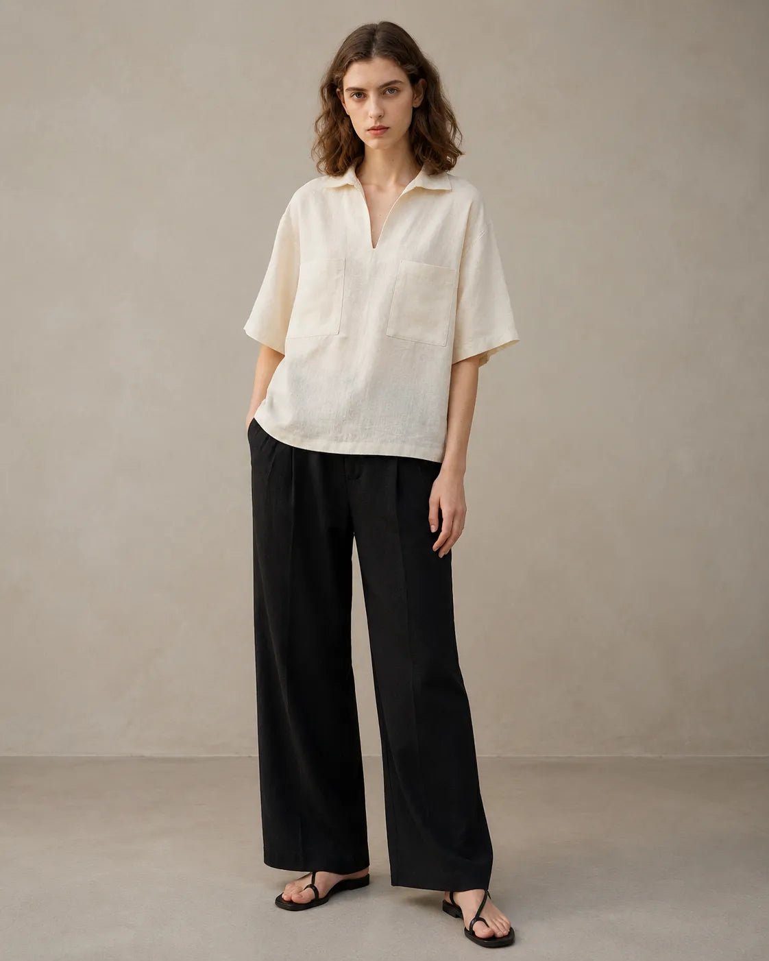 Full-length shot of a woman wearing an oversized off-white linen V-neck shirt, styled with wide-leg black trousers.