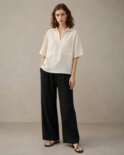 Full-length shot of a woman wearing an oversized off-white linen V-neck shirt, styled with wide-leg black trousers.