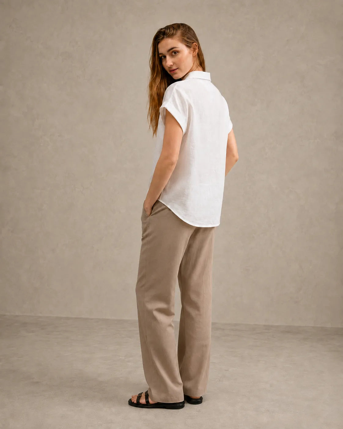 Three-quarter back view of a woman wearing a off-white linen shirt with a polo collar.