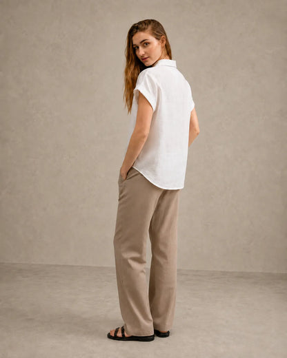Three-quarter back view of a woman wearing a off-white linen shirt with a polo collar.