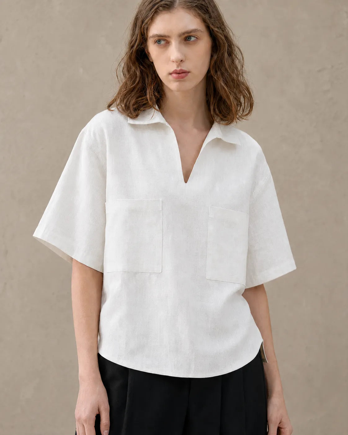 Close-up of the two patch pockets on an oversized off-white linen V-neck shirt.
