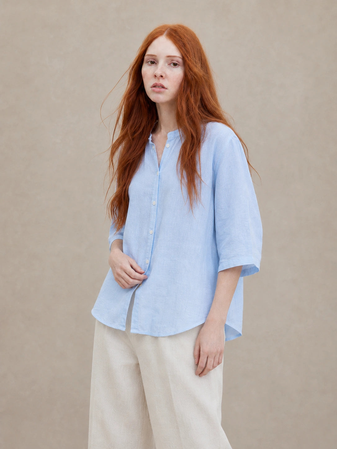Vrouw draagt een losvallende hemelsblauw linnen blouse met V-hals en driekwart mouwen, vooraanzicht.
