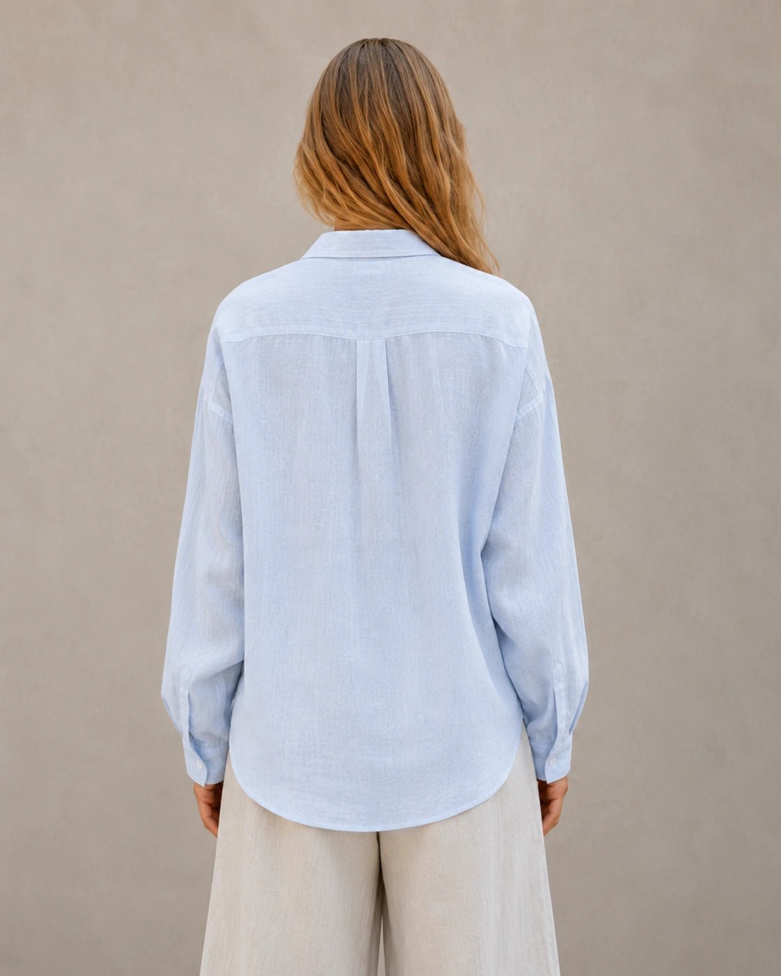 Driekwart achteraanzicht van een vrouw in een oversized ijsblauw linnen blouse.