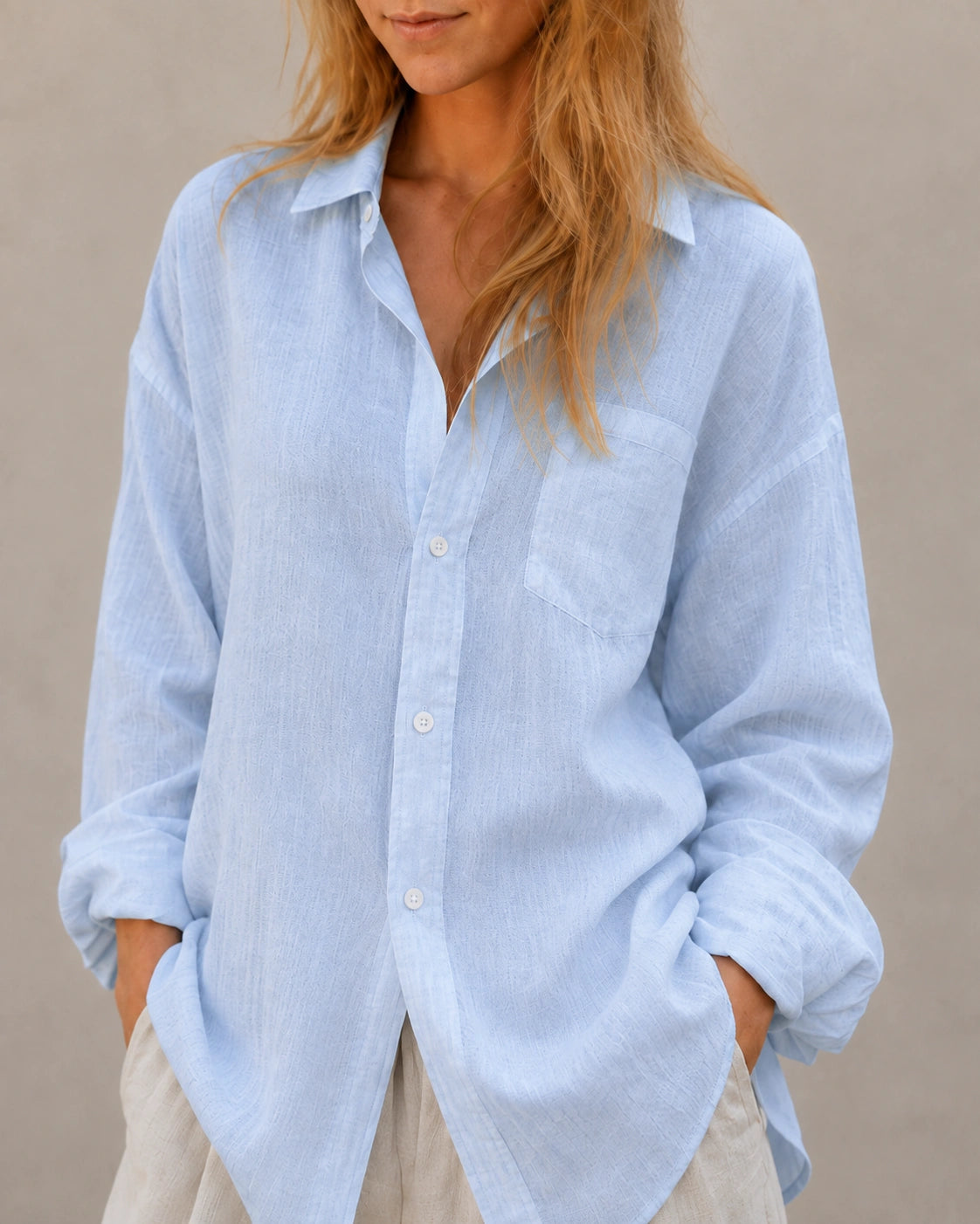 Close-up van de open kraag en halslijn van een oversized ijsblauw linnen blouse.