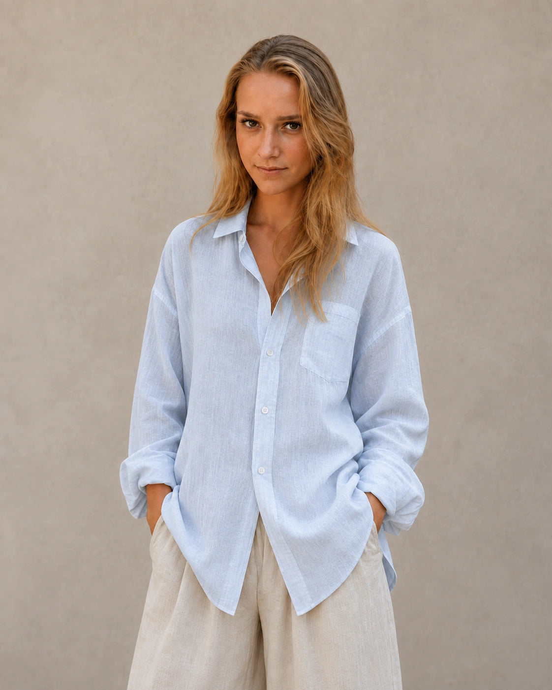 Vrouw draagt een oversized ijsblauw linnen blouse met reverskraag, handen in zakken, vooraanzicht.