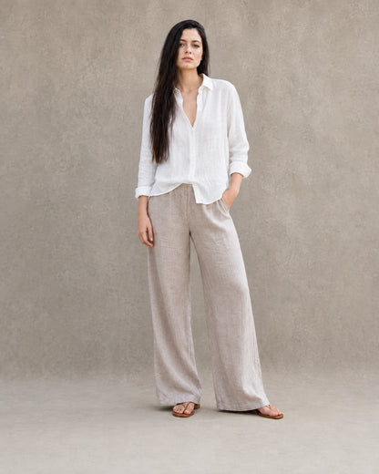 Volledige look van een vrouw in een losse wit linnen-katoenen blouse, gecombineerd met een wijde linnen broek.