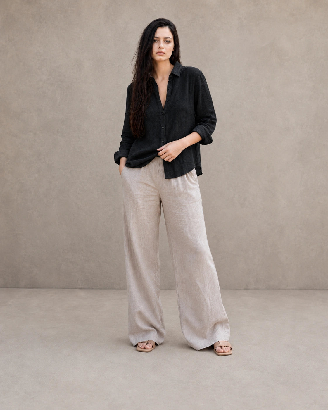 Volledige look van een vrouw in een losse zwart linnen-katoenen blouse, gecombineerd met een wijde linnen broek.