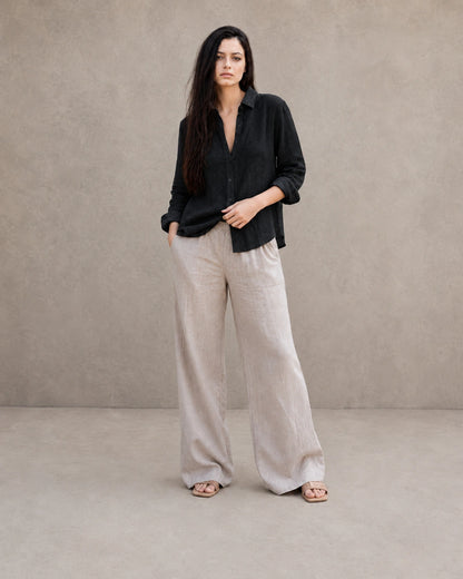 Volledige look van een vrouw in een losse zwart linnen-katoenen blouse, gecombineerd met een wijde linnen broek.
