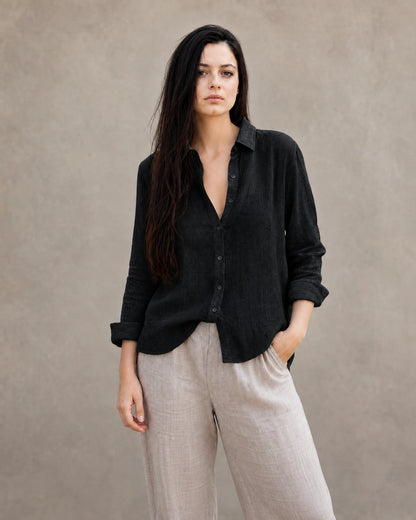 Vrouw draagt een losse zwart linnen-katoenen blouse met reverskraag en lange mouwen, vooraanzicht.
