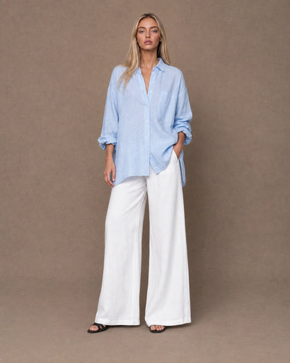 Volledige look van een vrouw in een relaxte lichtblauw linnen blouse, gecombineerd met een wijde broek.