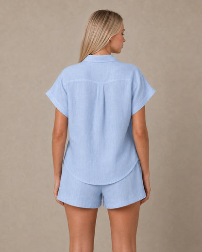 Achteraanzicht van een slank gesneden lichtblauw linnen blouse met korte mouwen.