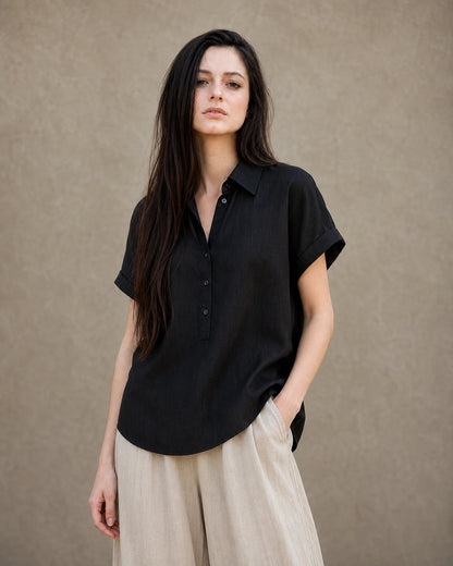 Vrouw draagt een zwart linnen-lyocell instapblouse met reverskraag en korte mouwen, vooraanzicht.