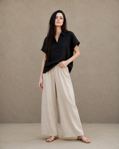 Volledige look van een vrouw in een zwart linnen-lyocell blouse, gecombineerd met een wijde linnen broek.