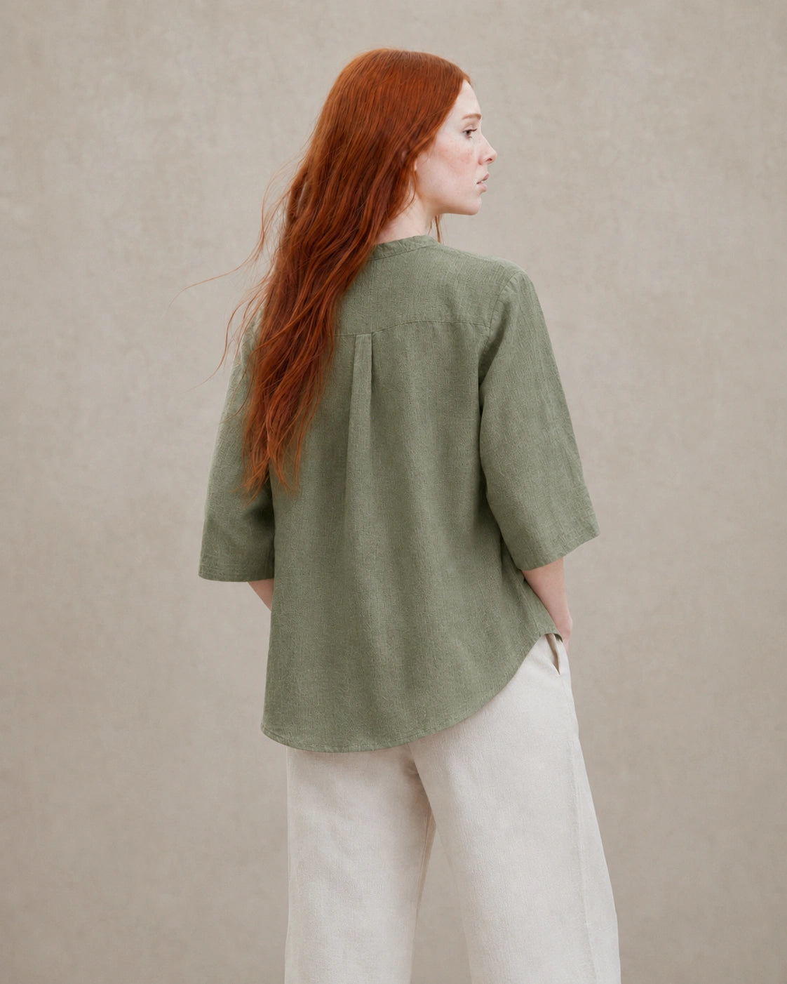 Driekwart achteraanzicht van een vrouw in een losvallende mosgroen linnen blouse.