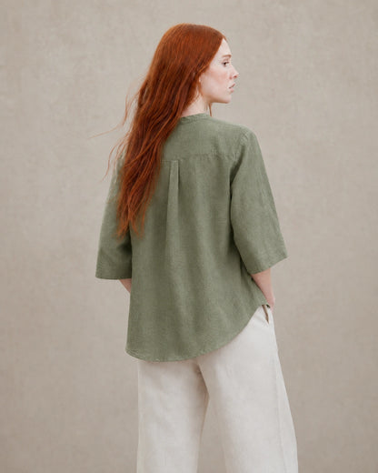 Driekwart achteraanzicht van een vrouw in een losvallende mosgroen linnen blouse.