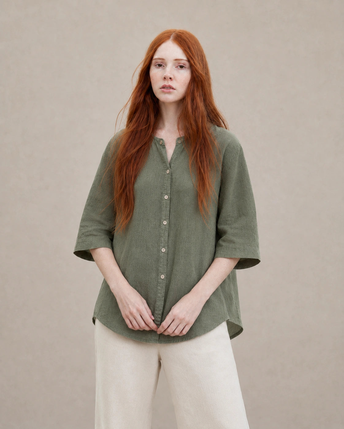 Vrouw draagt een losvallende mosgroen linnen blouse met V-hals en driekwart mouwen, vooraanzicht.