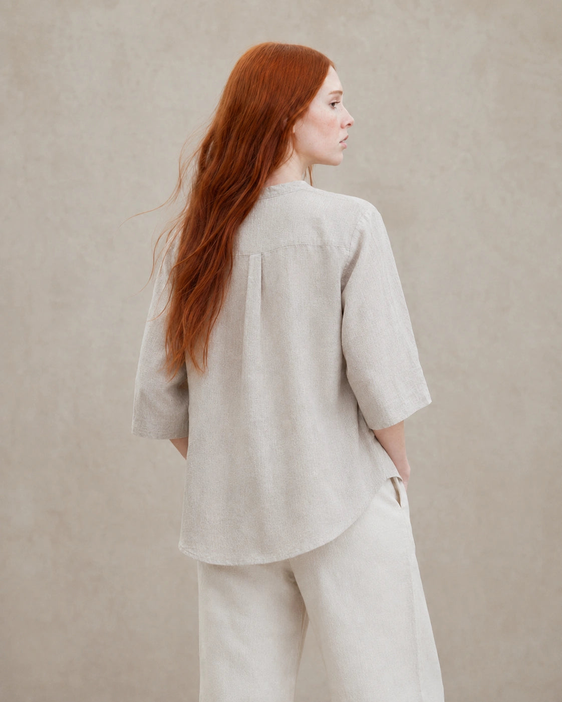 Driekwart achteraanzicht van een vrouw in een losvallende naturel linnen blouse.