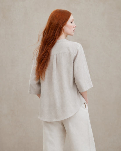 Driekwart achteraanzicht van een vrouw in een losvallende naturel linnen blouse.