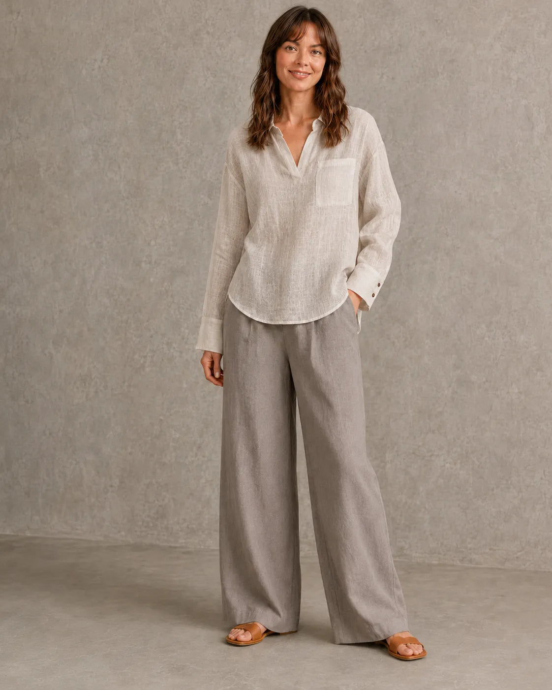 Volledige look van een vrouw in een naturel linnen blouse met getailleerde taille, gecombineerd met een wijde broek.