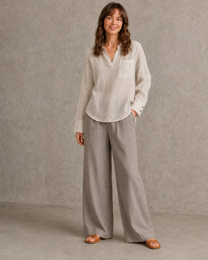 Volledige look van een vrouw in een naturel linnen blouse met getailleerde taille, gecombineerd met een wijde broek.