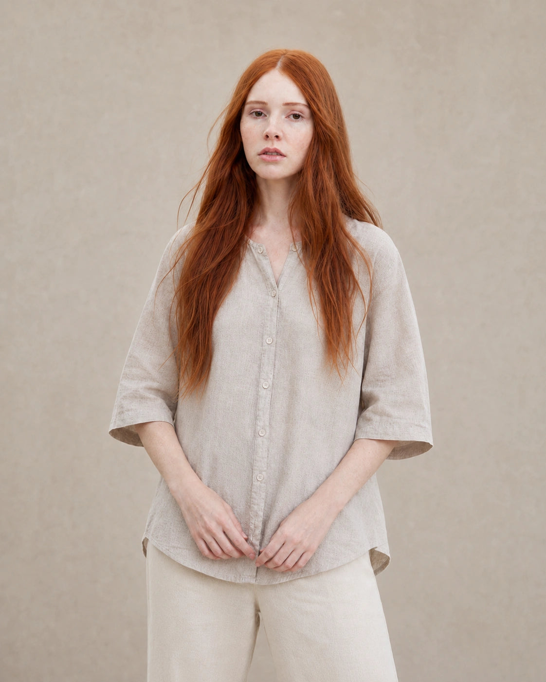 Vrouw draagt een losvallende naturel linnen blouse met V-hals en driekwart mouwen, vooraanzicht.