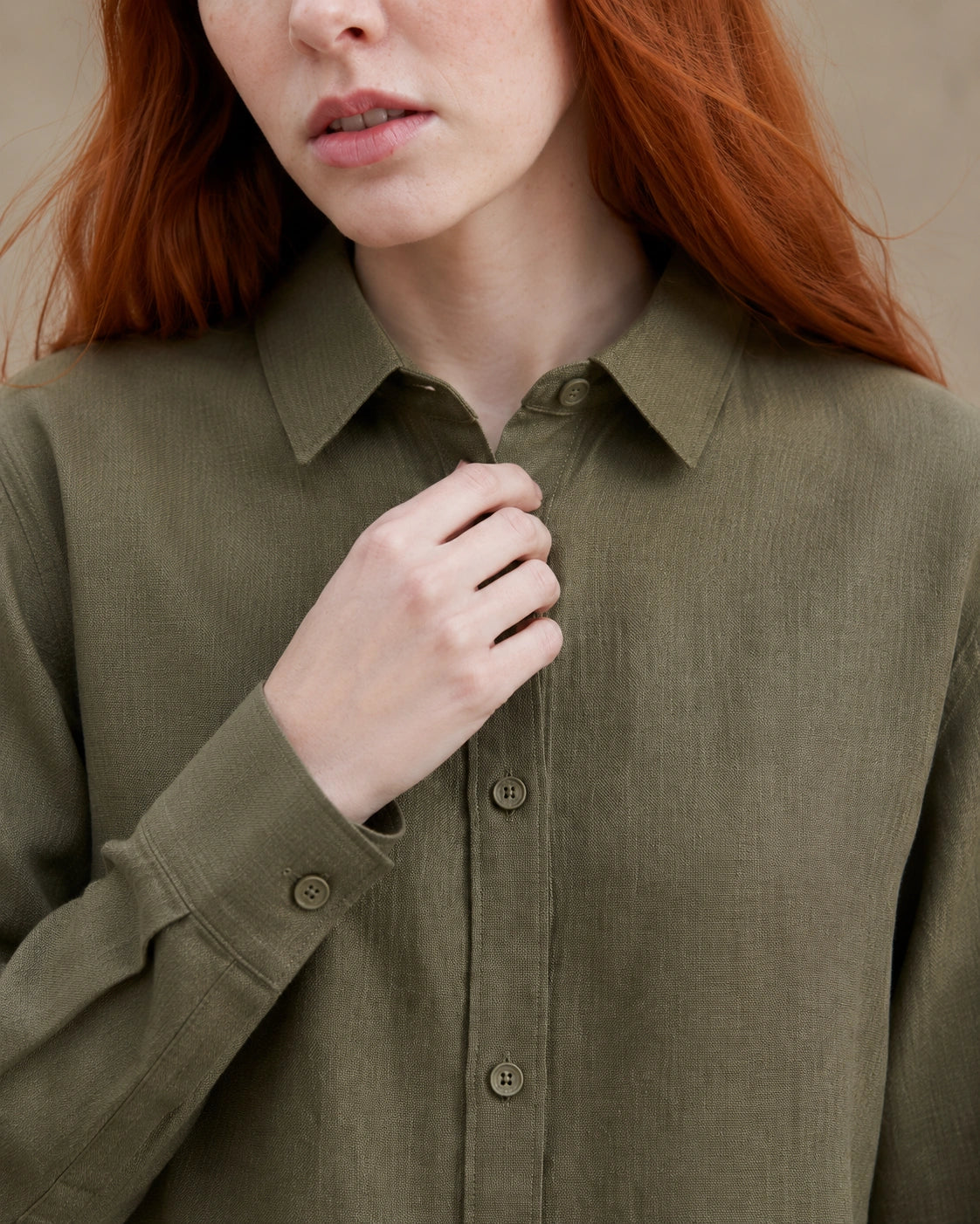 Close-up van de getailleerde kraag en knopenlijst van een olijfgroen linnen blouse.