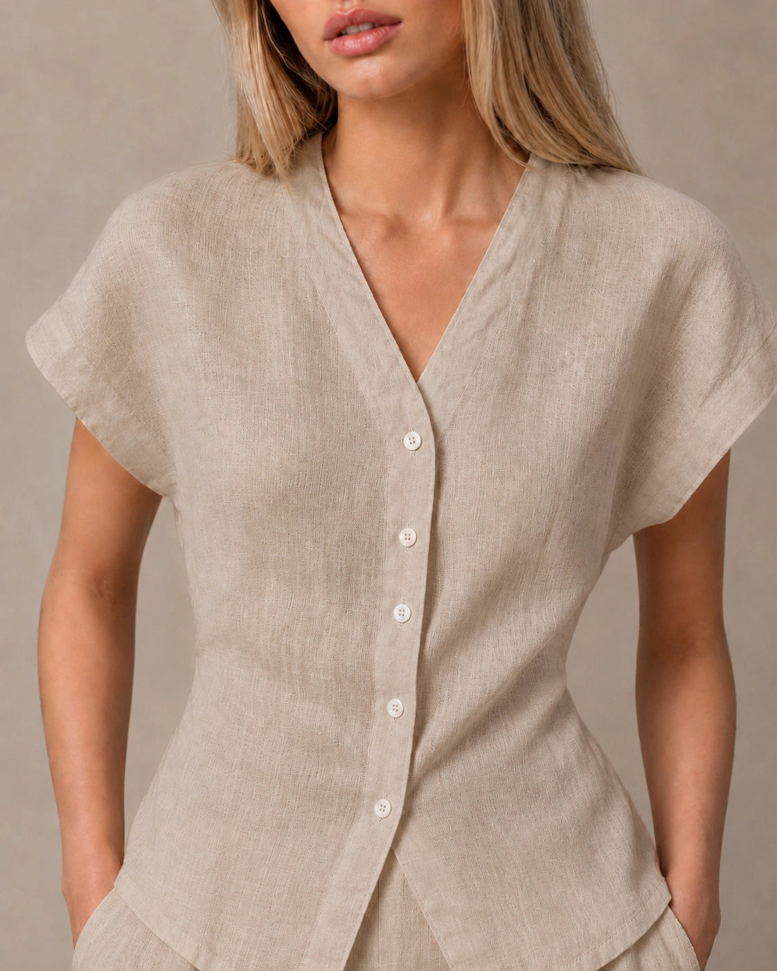 Close-up van de gedrapeerde, geplooide voorkant van een slank gesneden taupe linnen blouse.