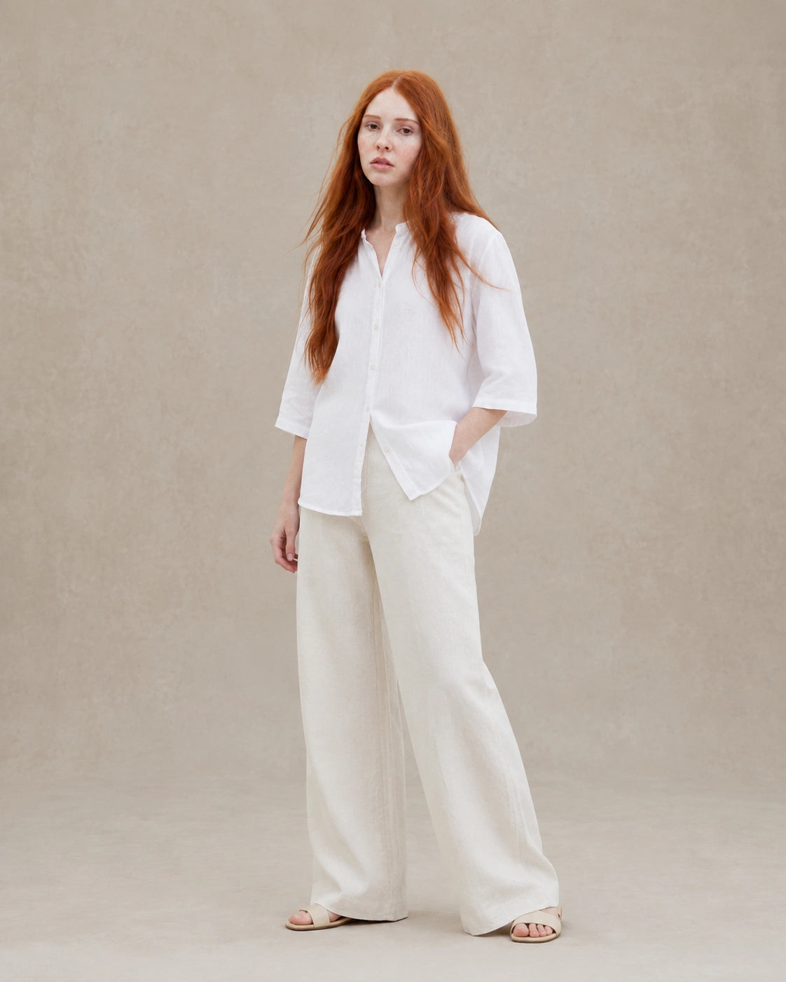 Volledige look van een vrouw in een losvallende wit linnen blouse, gecombineerd met een wijde crème broek.