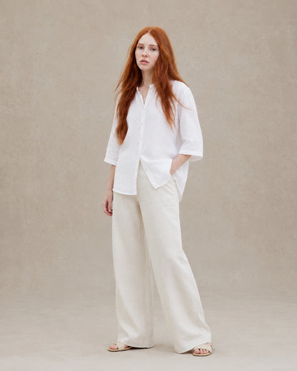 Volledige look van een vrouw in een losvallende wit linnen blouse, gecombineerd met een wijde crème broek.
