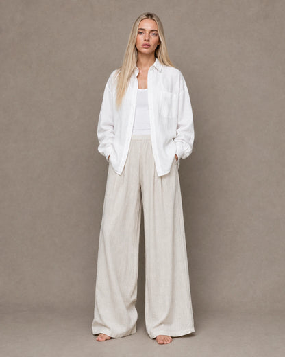 Full-length shot of a woman wearing a white linen shirt open over trousers in a matching tone.