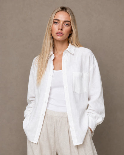 Woman wearing an open, cardigan-style white linen shirt with a polo collar over a white camisole.