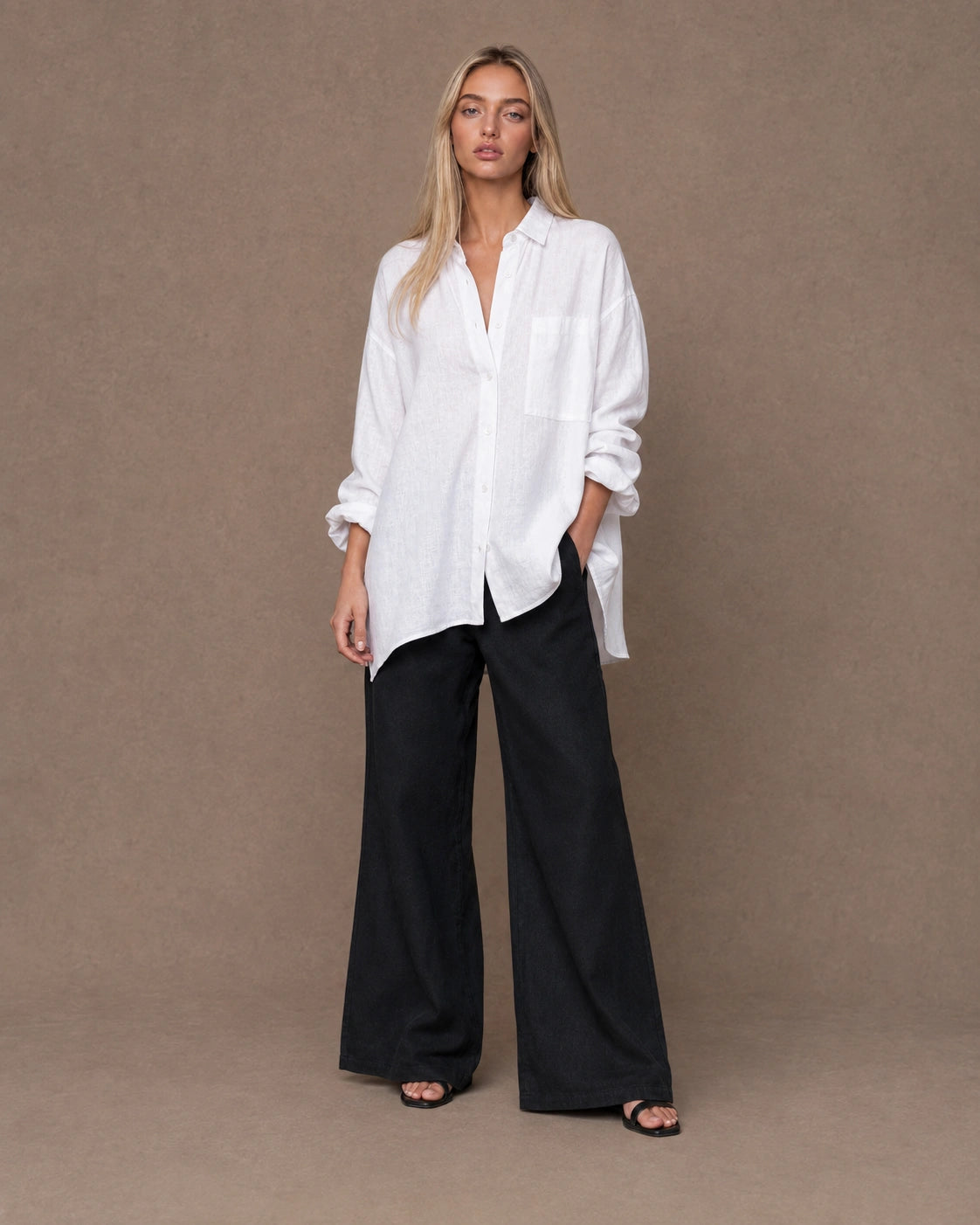 Volledige look van een vrouw in een relaxte wit linnen blouse, gecombineerd met een wijde broek.