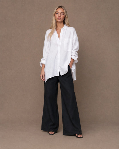 Volledige look van een vrouw in een relaxte wit linnen blouse, gecombineerd met een wijde broek.